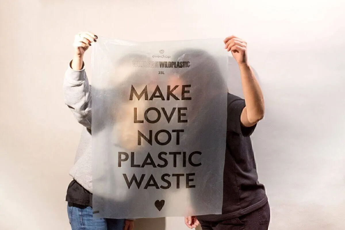 Zwei Personen halten eine transparente everdrop-WILDBAG vor ihre Gesichter, darauf in großen Versalien „MAKE LOVE NOT PLASTIC WASTE“ mit Herz-Symbol